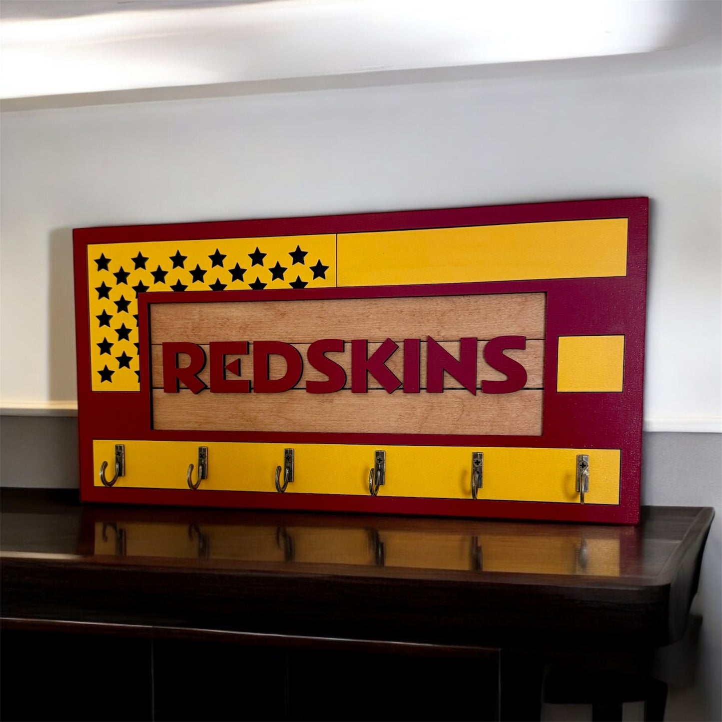 USA flag-inspired wooden key holder with “Redskins” in maroon letters, featuring yellow and maroon accents, six metal hooks, and a rustic maple wood background.