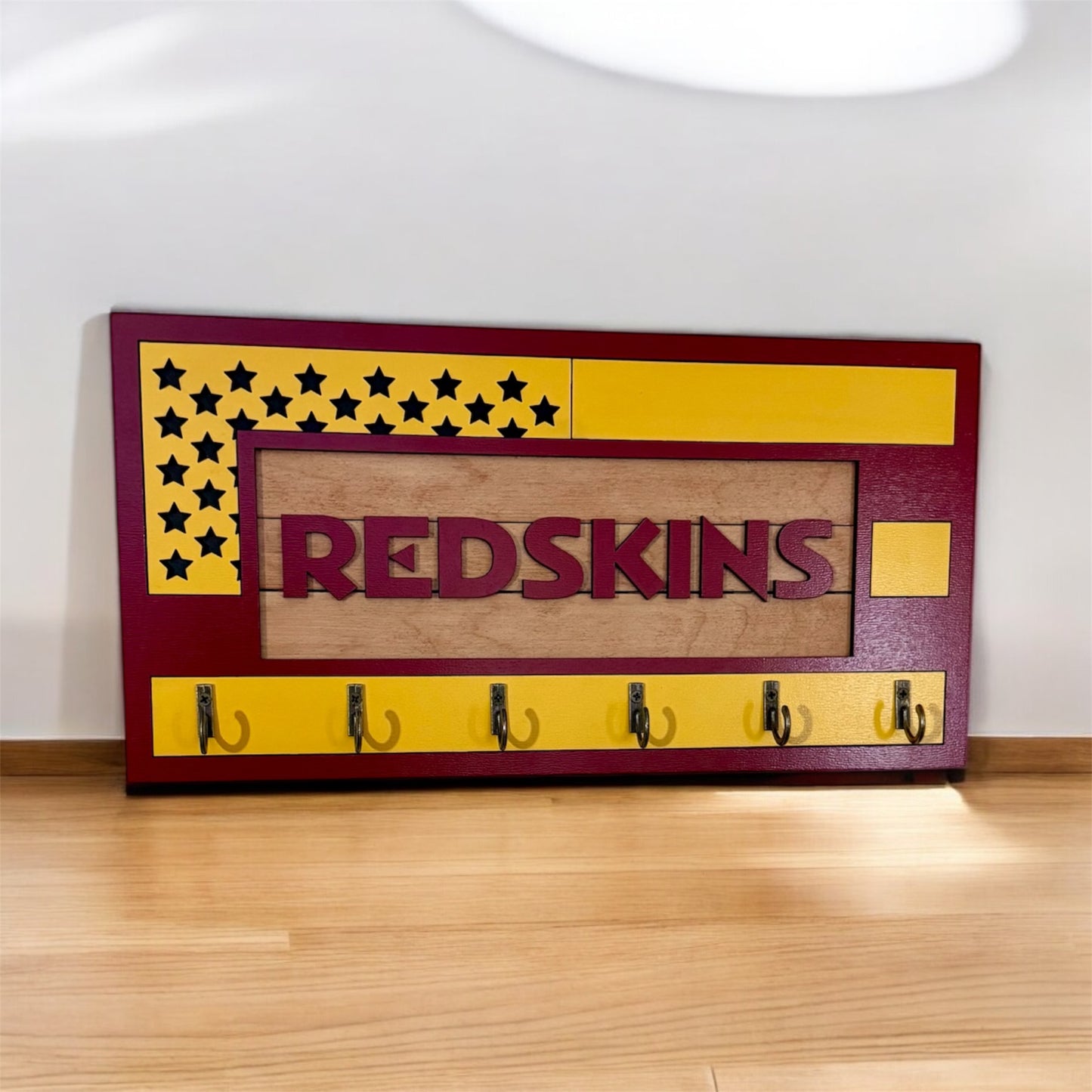 USA flag-inspired wooden key holder with “Redskins” in maroon letters, featuring yellow and maroon accents, six metal hooks, and a rustic maple wood background.