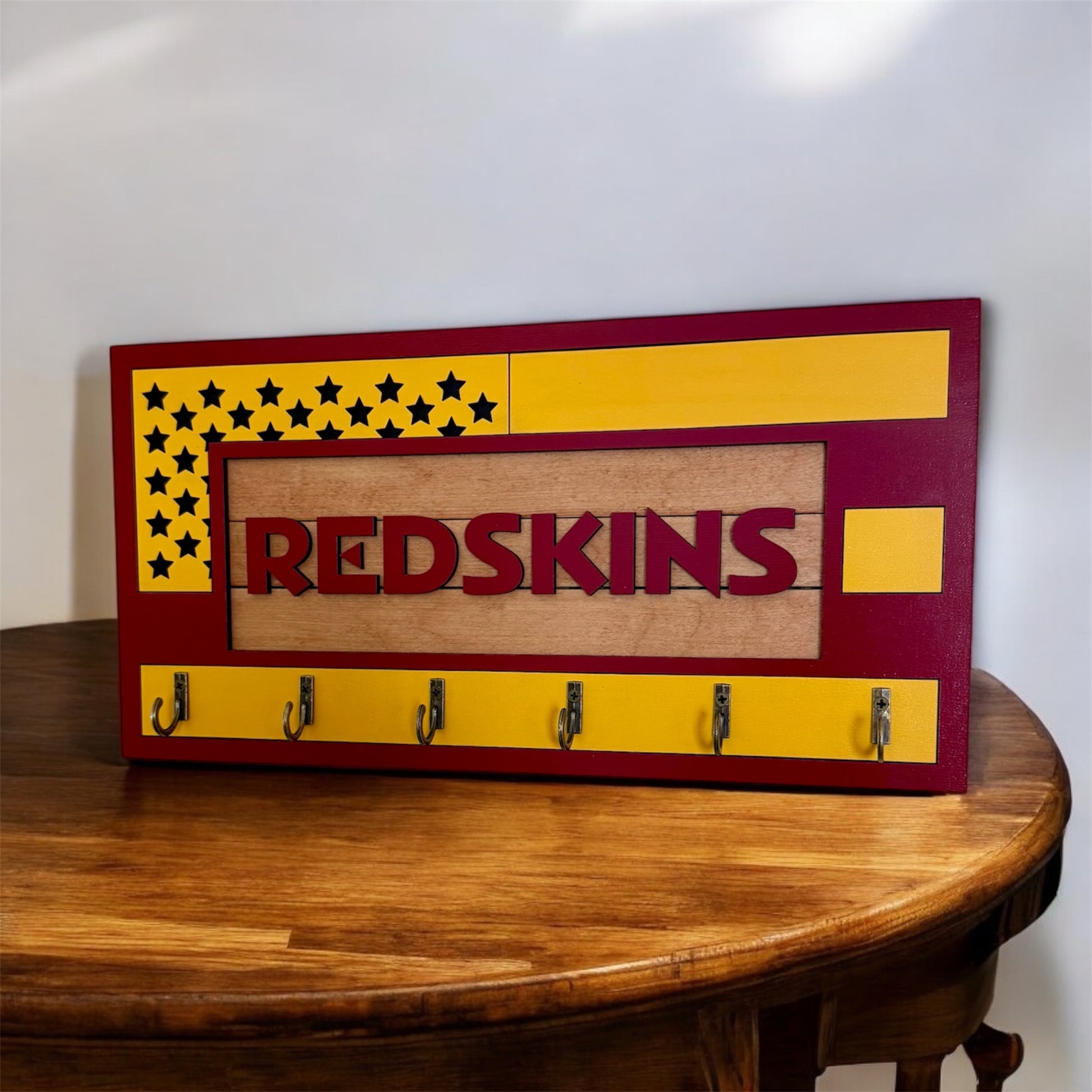 USA flag-inspired wooden key holder with “Redskins” in maroon letters, featuring yellow and maroon accents, six metal hooks, and a rustic maple wood background.