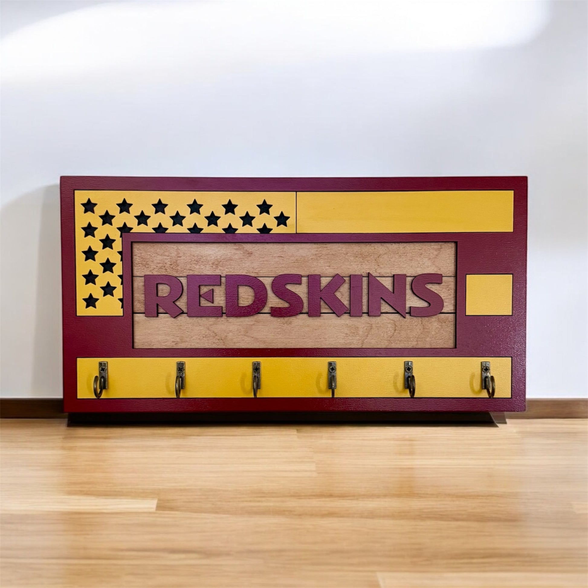 USA flag-inspired wooden key holder with “Redskins” in maroon letters, featuring yellow and maroon accents, six metal hooks, and a rustic maple wood background.
