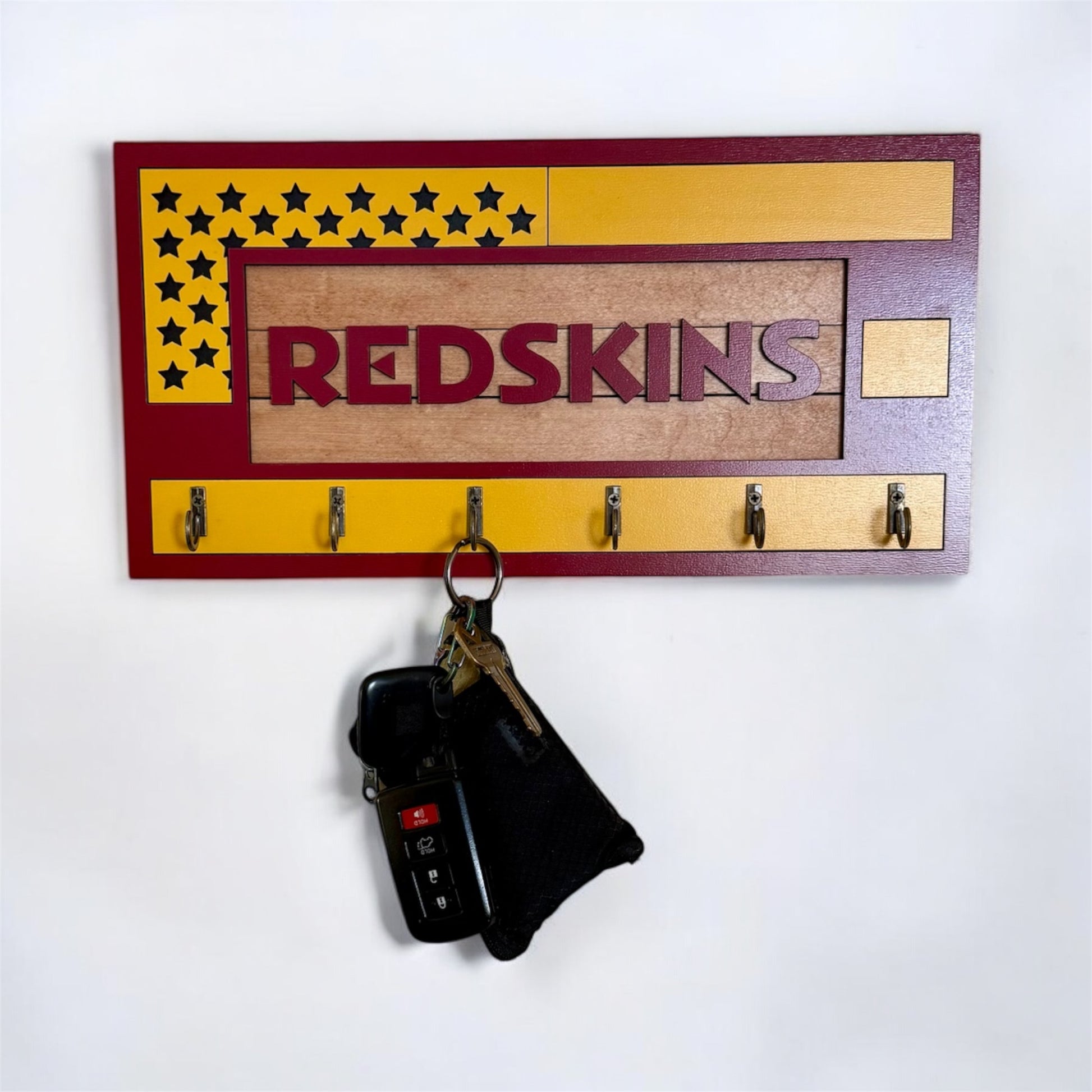 USA flag-inspired wooden key holder with “Redskins” in maroon letters, featuring yellow and maroon accents, six metal hooks, and a rustic maple wood background.