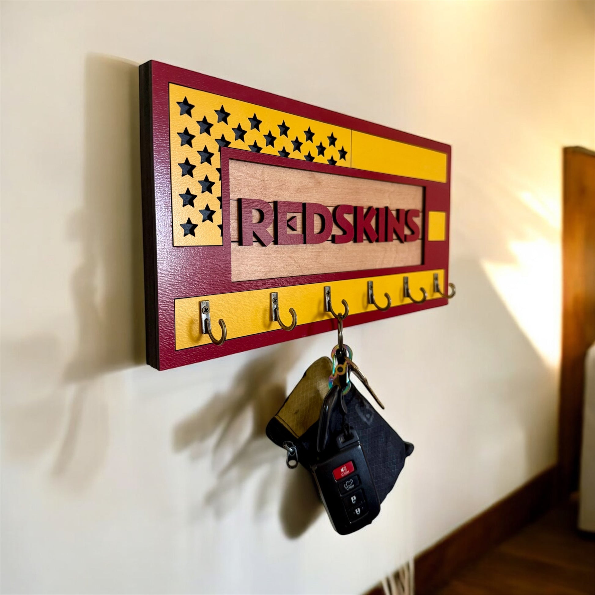USA flag-inspired wooden key holder with “Redskins” in maroon letters, featuring yellow and maroon accents, six metal hooks, and a rustic maple wood background.