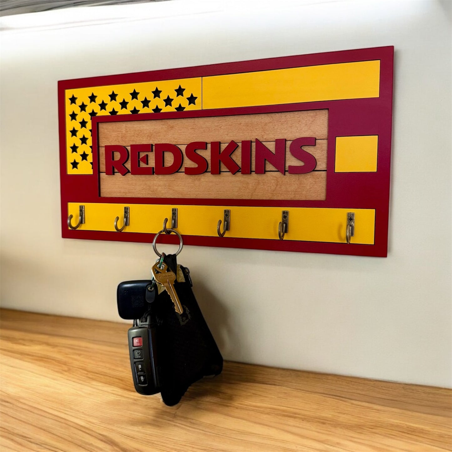 USA flag-inspired wooden key holder with “Redskins” in maroon letters, featuring yellow and maroon accents, six metal hooks, and a rustic maple wood background.