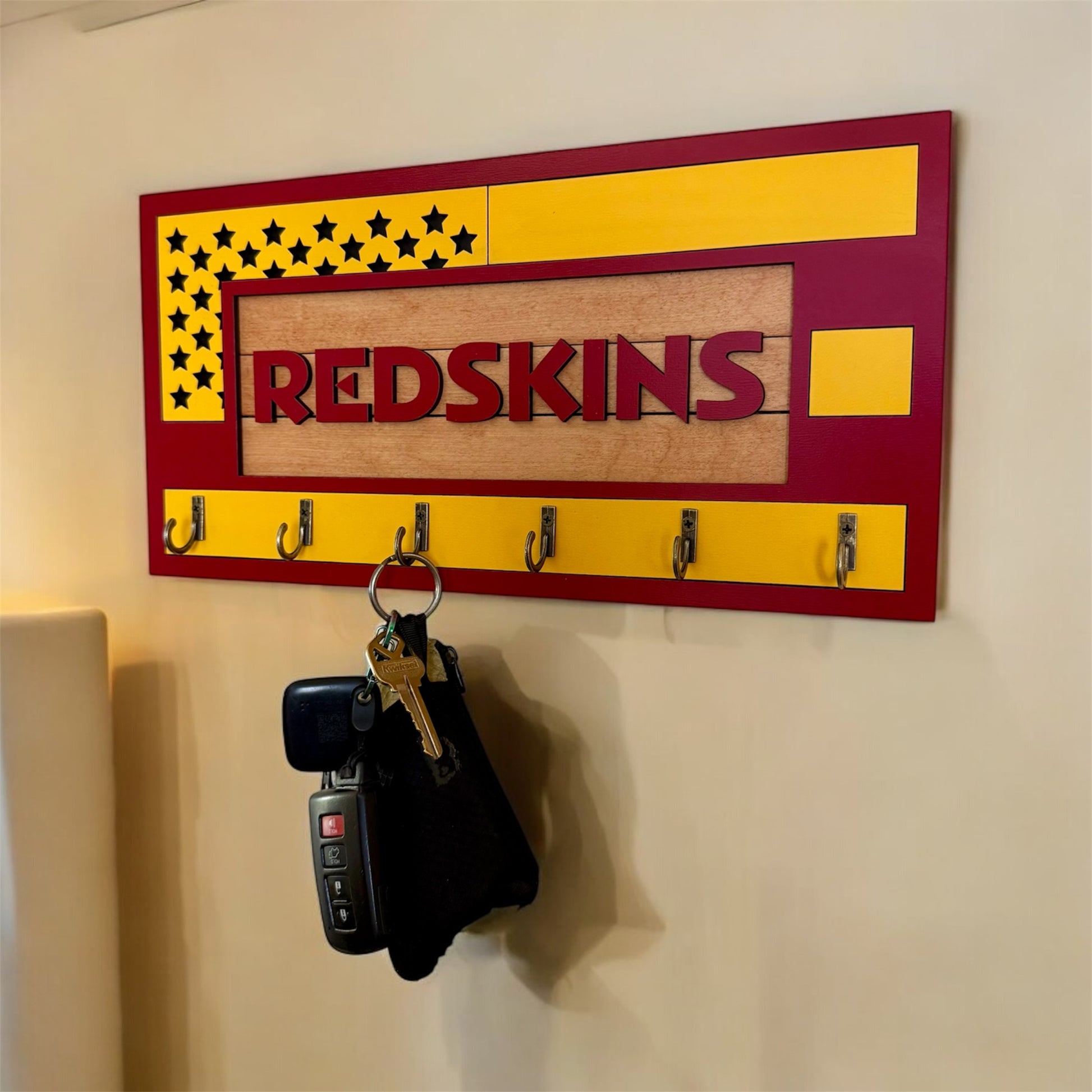 USA flag-inspired wooden key holder with “Redskins” in maroon letters, featuring yellow and maroon accents, six metal hooks, and a rustic maple wood background.